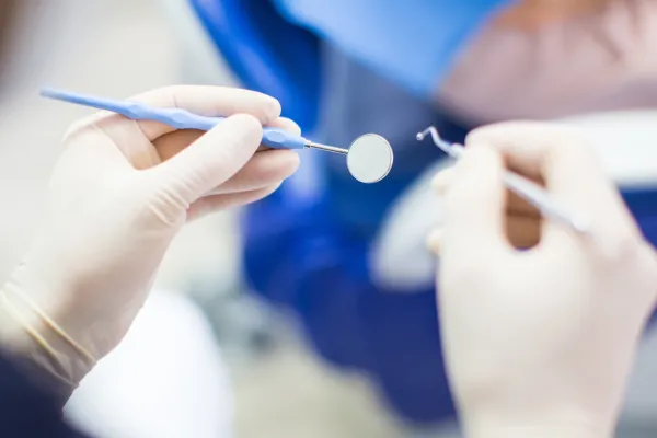 Stock image of a pair of hands wearing medical gloves and holding dental tools. Photo credit: Getty Images/Luis Alvarez